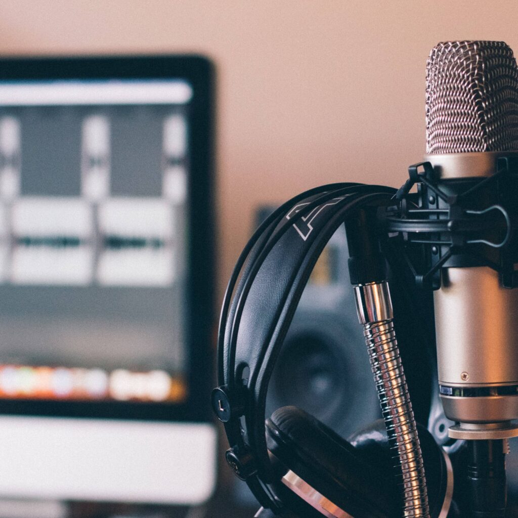Mikrofon i słuchawki na pierwszym planie a w tle widoczny monitor (podcast co to jest)